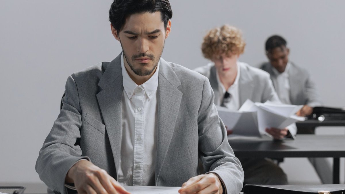 Serious businessmen in gray suits reviewing documents in an office environment.