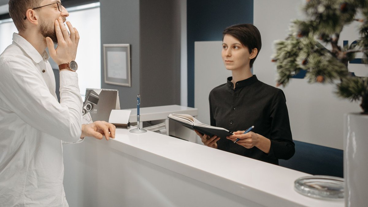 A receptionist assists a patient with a toothache at a dental clinic's front desk.