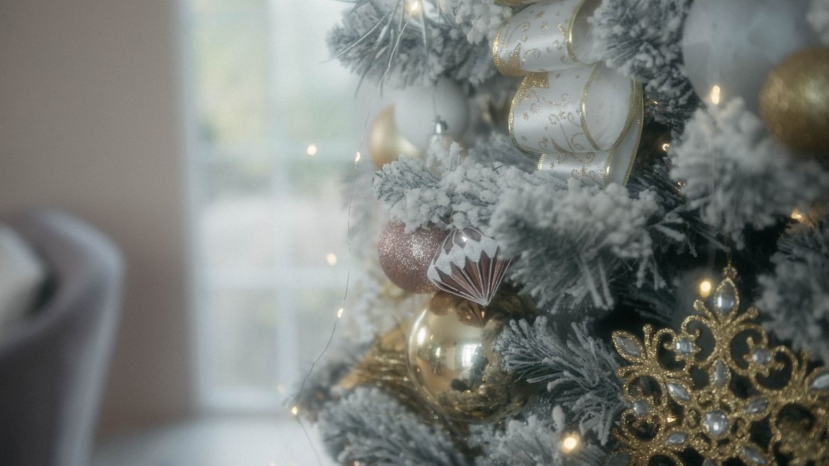 A beautifully decorated Christmas tree with gold and white ornaments, ribbon, and lights indoors.