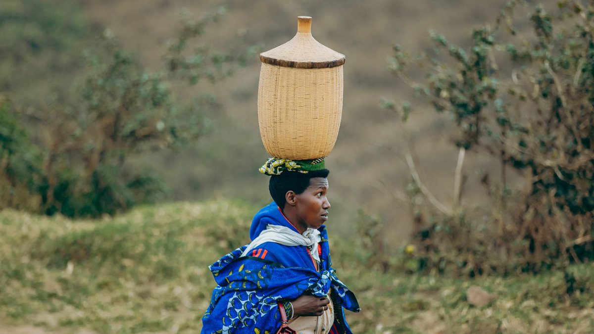 Maintel Chief People Officer emphasizes empowering managers African woman in traditional clothing carrying basket on head along rural path.