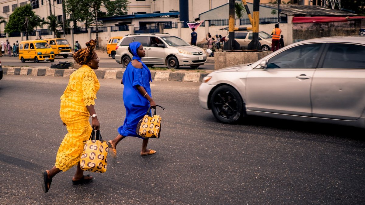 Two women in traditional Nigerian outfits cross a bustling street in Lagos, Nigeria.