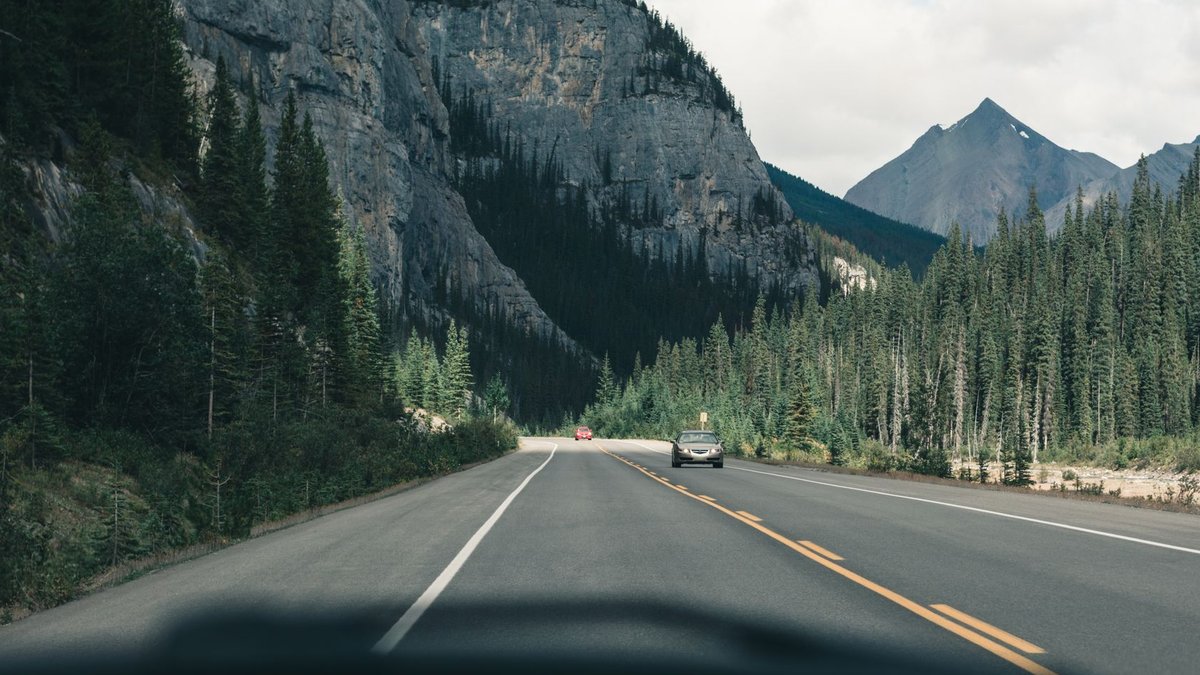 Scenic view of a quiet mountain road in Canada, surrounded by lush forests and towering peaks.