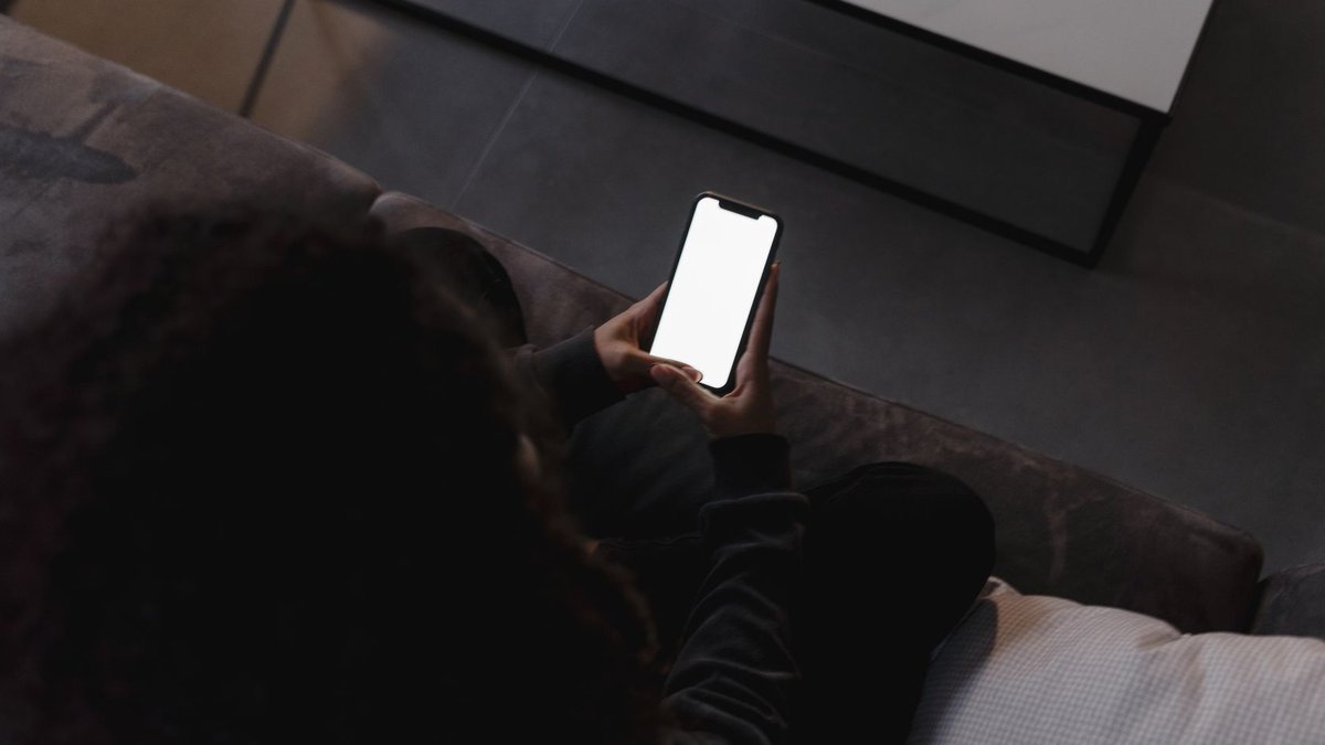 Safaricom Expands M-PESA Payment Options A person holding a smartphone with a blank screen, seated indoors on a couch.