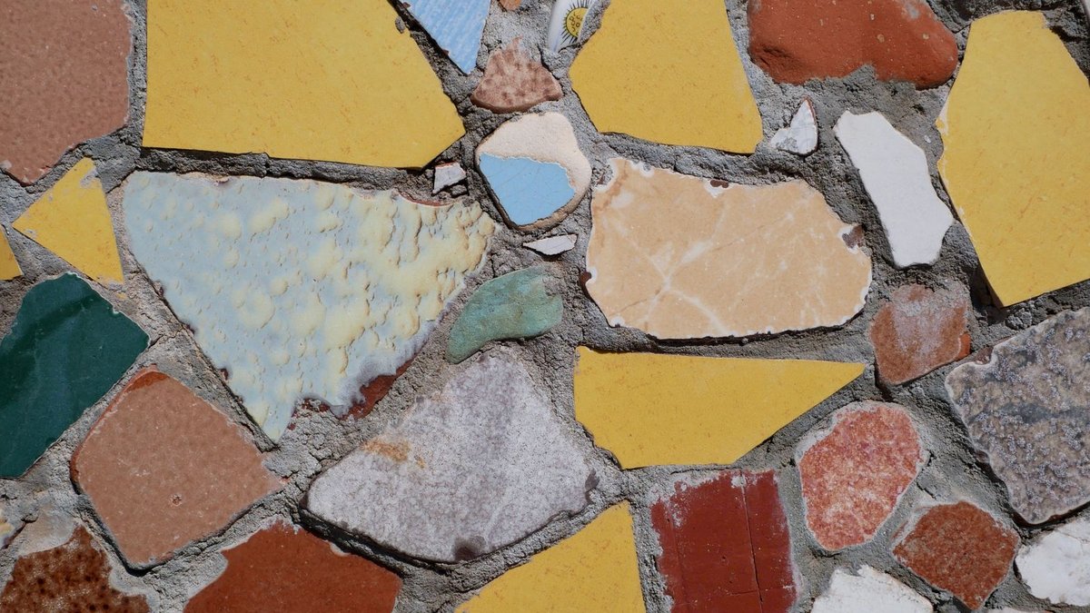 Shaw Contract Launches 'Simply in Motion' Carpet Tile Collection Vibrant mosaic of broken tiles in various colors and shapes, forming a textured wall pattern.