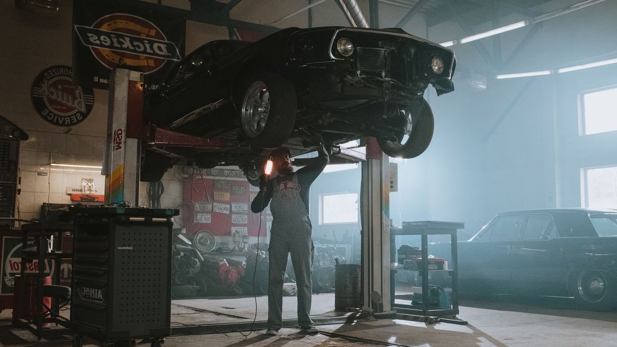 Top Gear Tech Launches YouTube Channel on Automotive Innovation Male mechanic using a light to inspect a classic car lifted in an automotive garage.