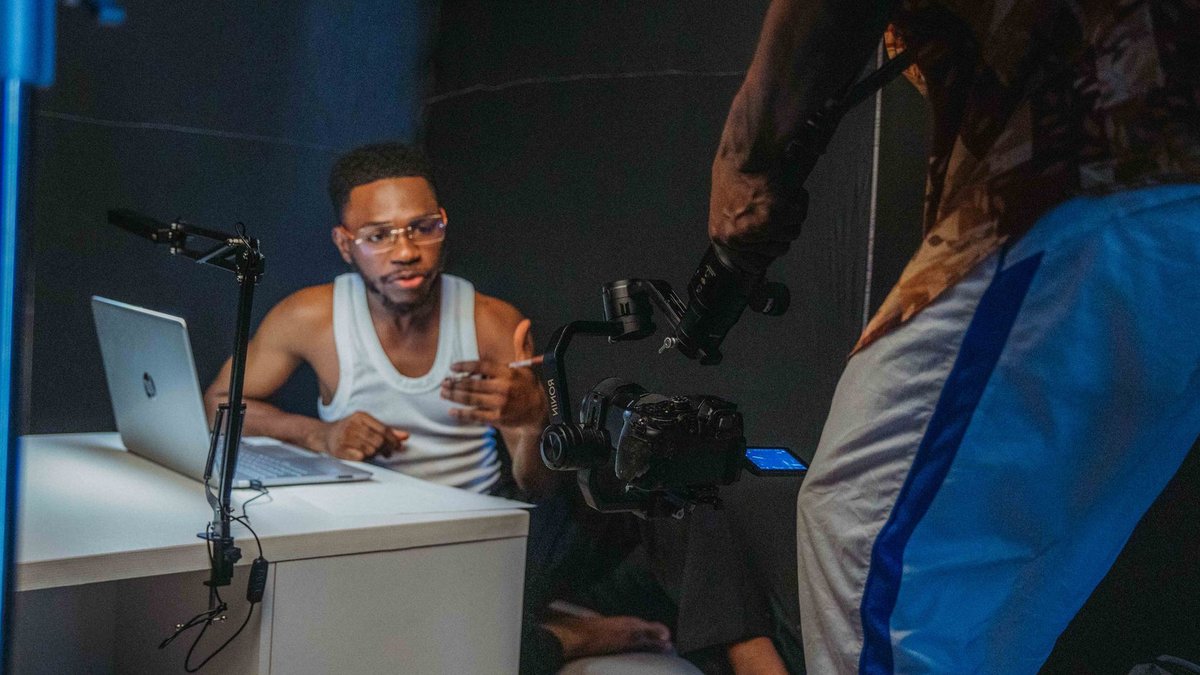 Young black men filming a casual video with laptop and camera in a home studio setting.