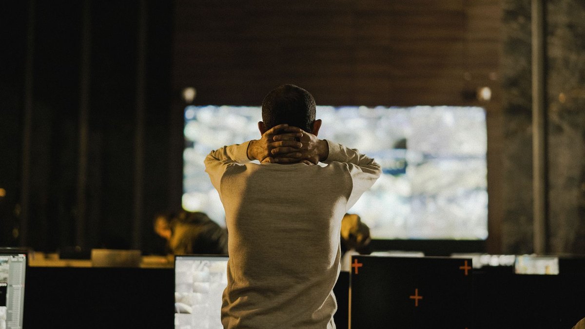 Retailers and police join to fight crime A man stands thoughtfully in a dimly lit control room with various screens.