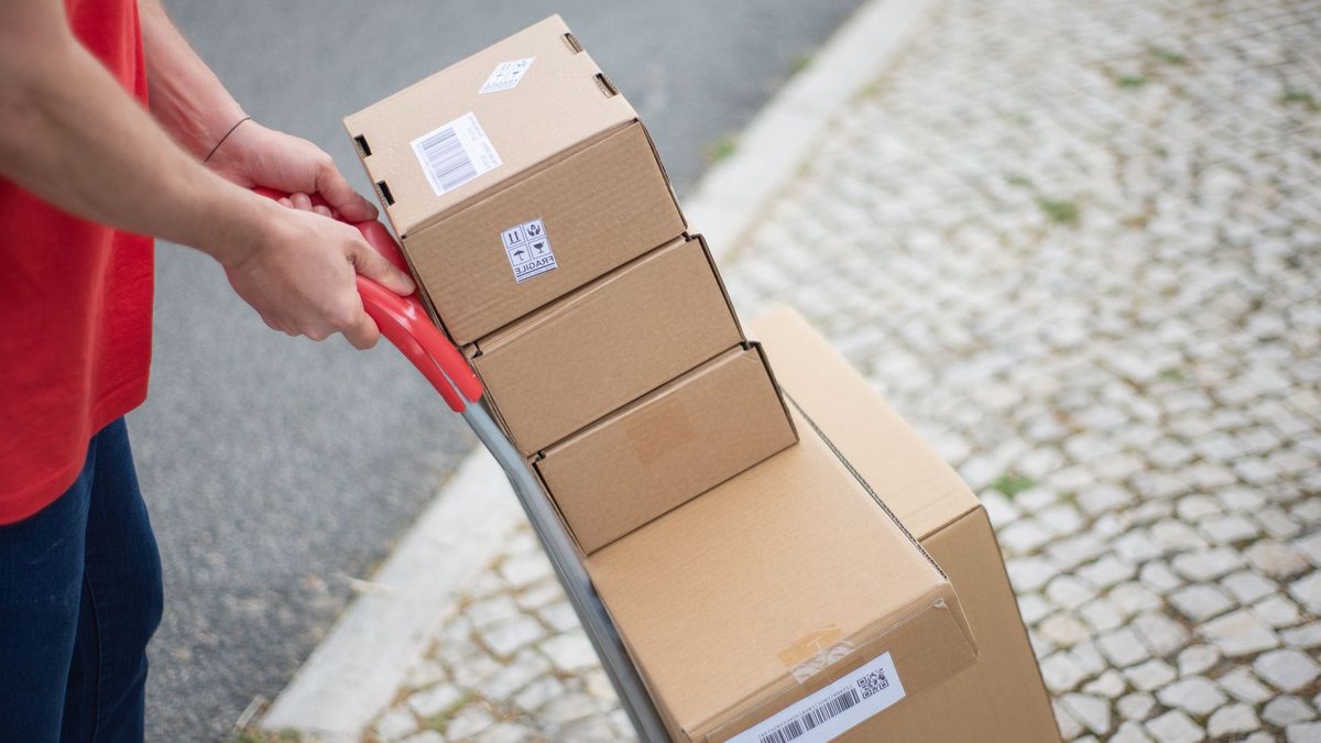 EU Shoppers Face New €2 Fee on Non-EU Parcels Courier handling packages with a cart on a cobblestone street in daylight.
