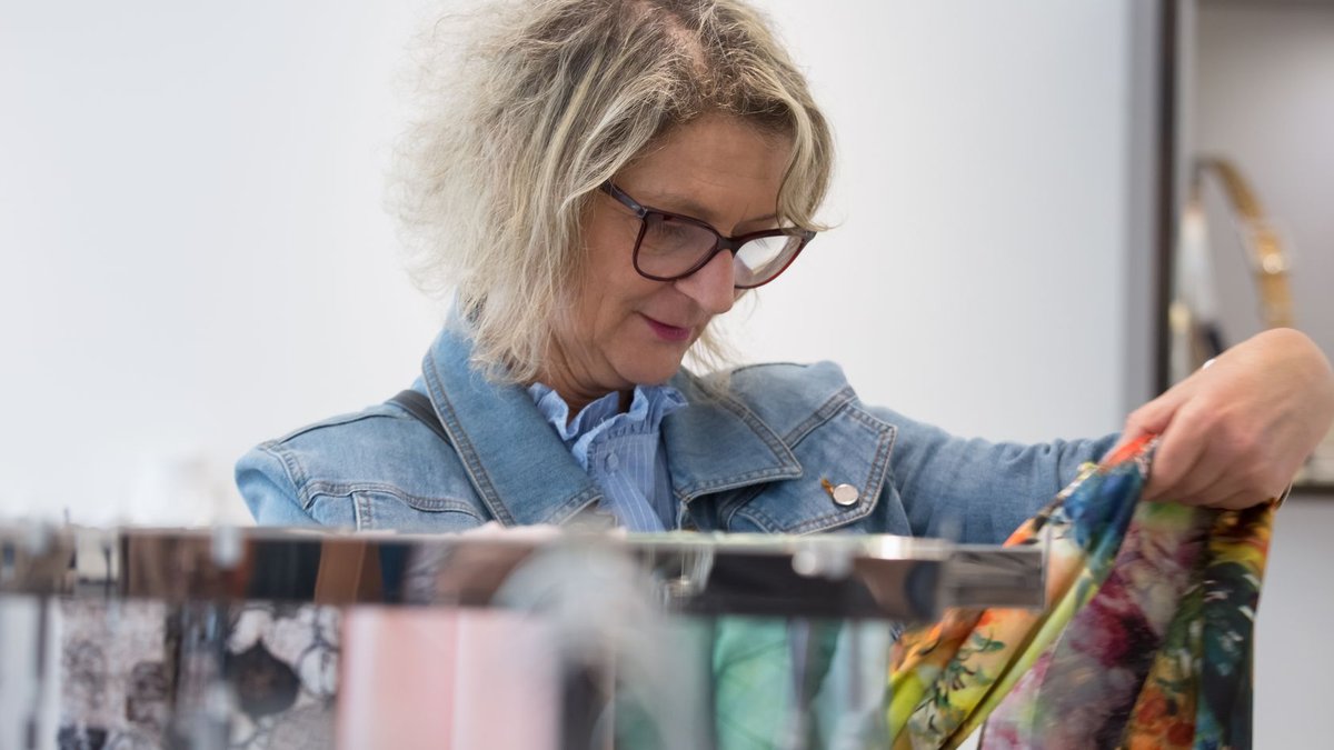Elderly woman with glasses chooses vibrant scarves in a store.