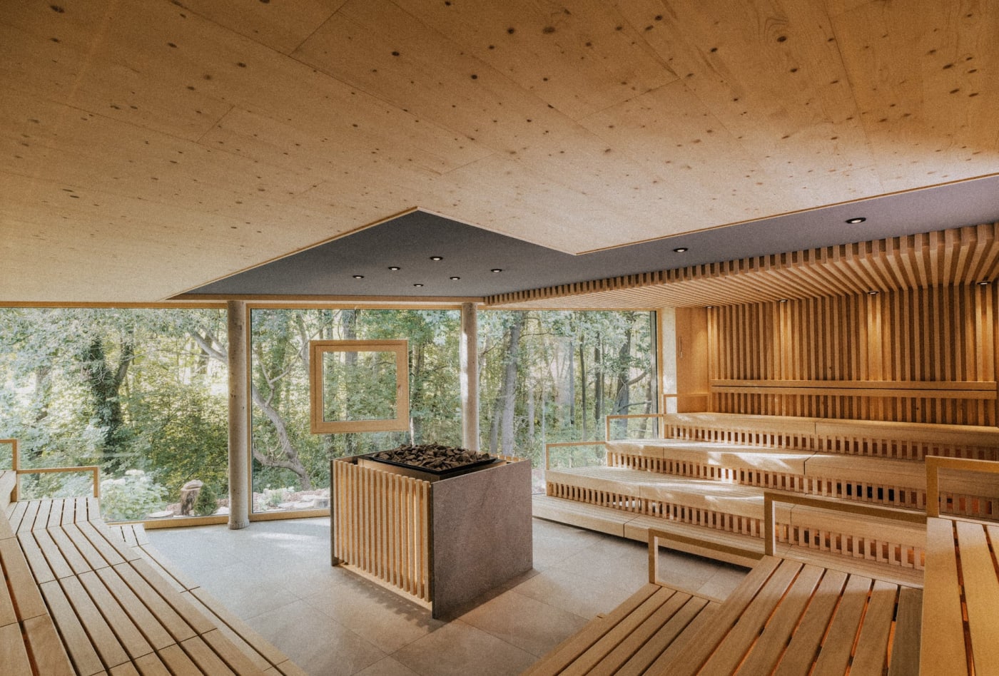 Les gradins en bois clair et le poêle central du Quell-Sauna, face aux baies vitrées ouvertes sur la forêt