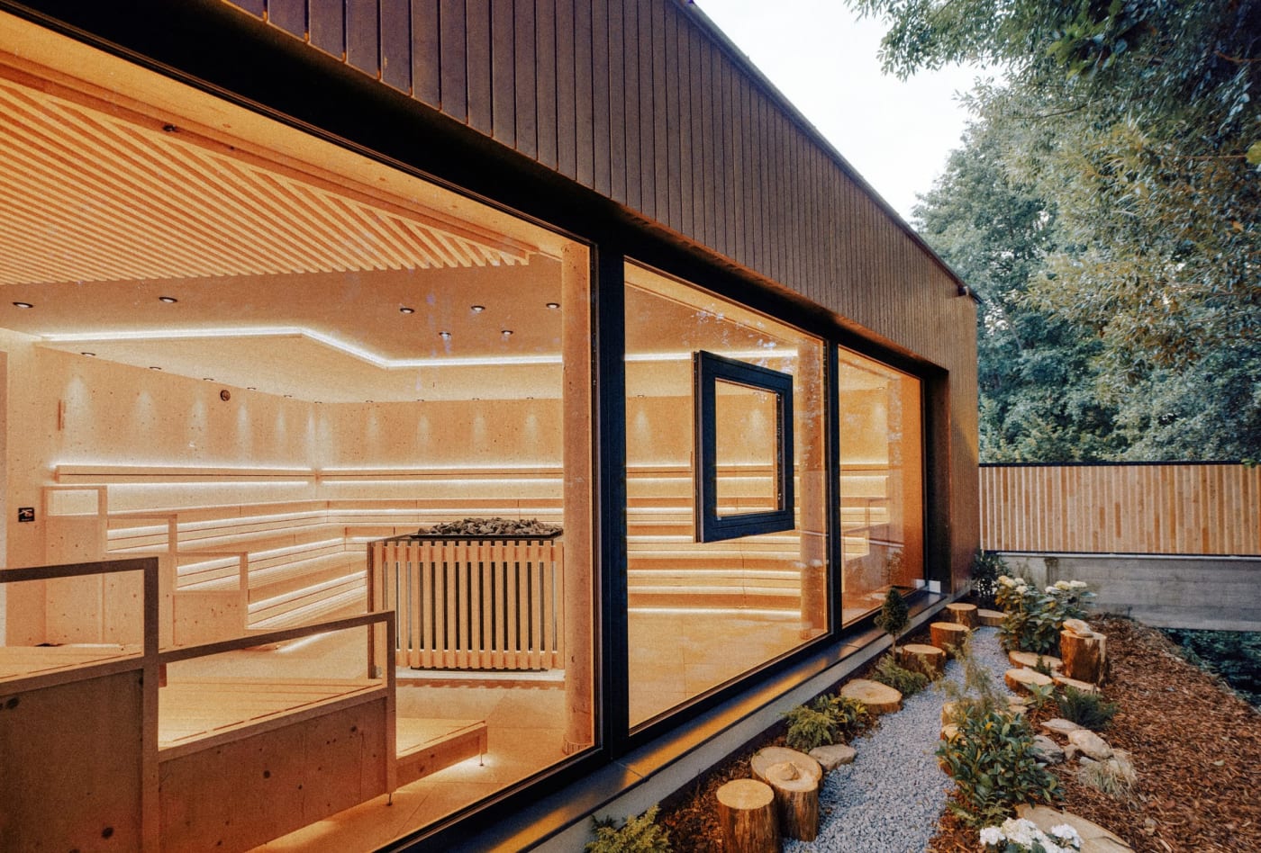 Le bardage en bois et les grandes baies vitrées du Quell-Sauna, gradins éclairés