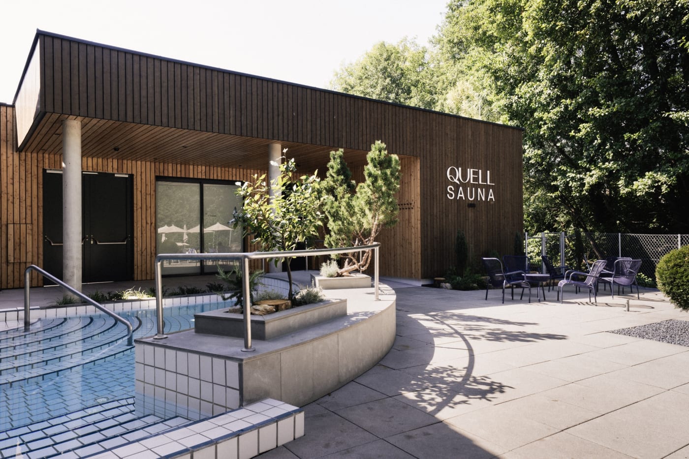 L'entrée du Quell-Sauna, sa façade en bois sombre et sa terrasse au bord du bassin extérieur