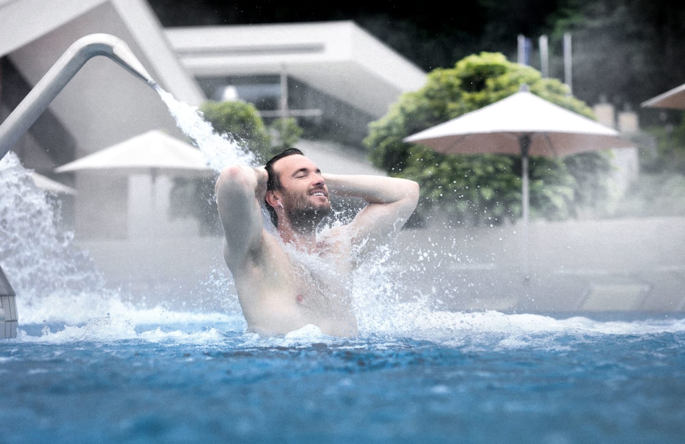Un baigneur sous une cascade d'eau thermale dans le bassin de massage extérieur