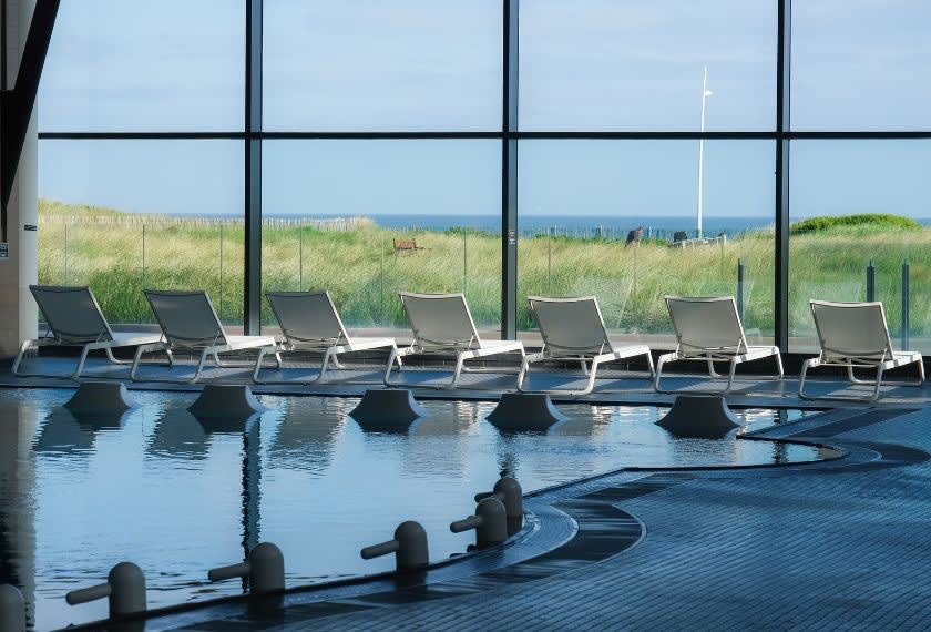 Le bassin d'eau de mer intérieur du Thalazur Cabourg et ses transats, derrière une verrière ouverte sur les dunes