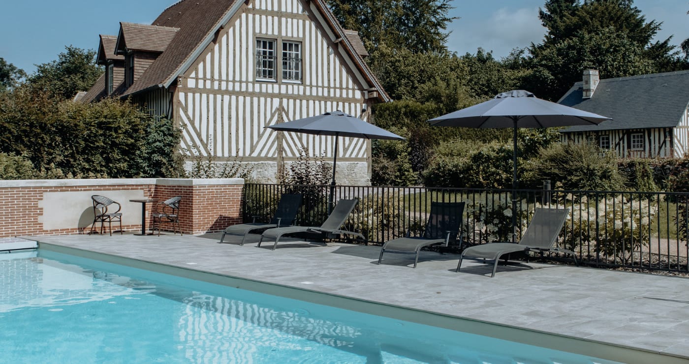 La piscine extérieure chauffée des Manoirs des Portes de Deauville devant un cottage à colombages, à Canapville