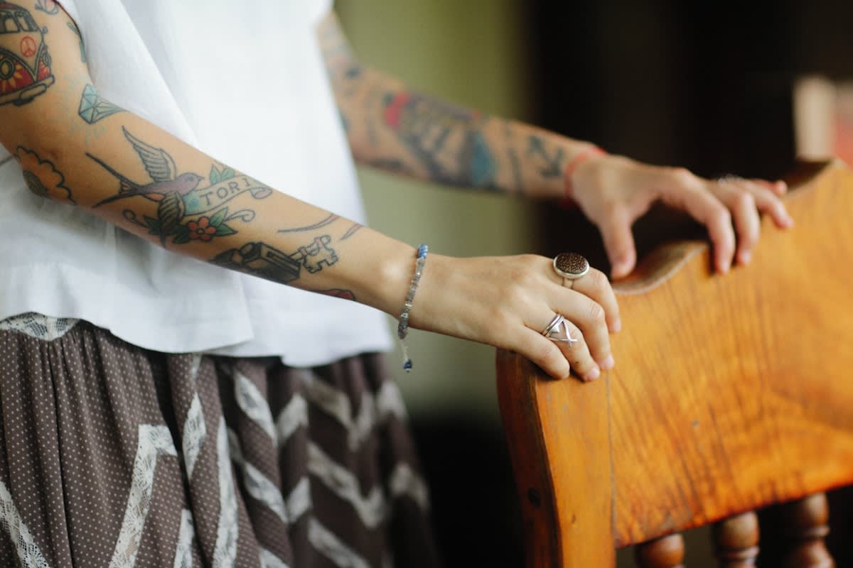 woman with tattoos on her arm holding a wooden chair
