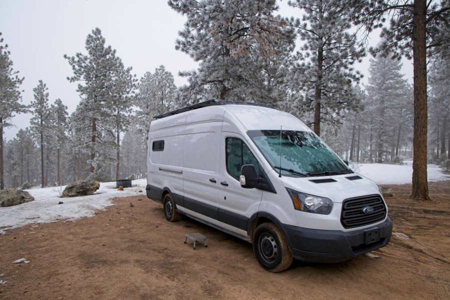 Campervan parked in a camping spot within the Pike National Forest.  Snow is covering the ground around the campsite.