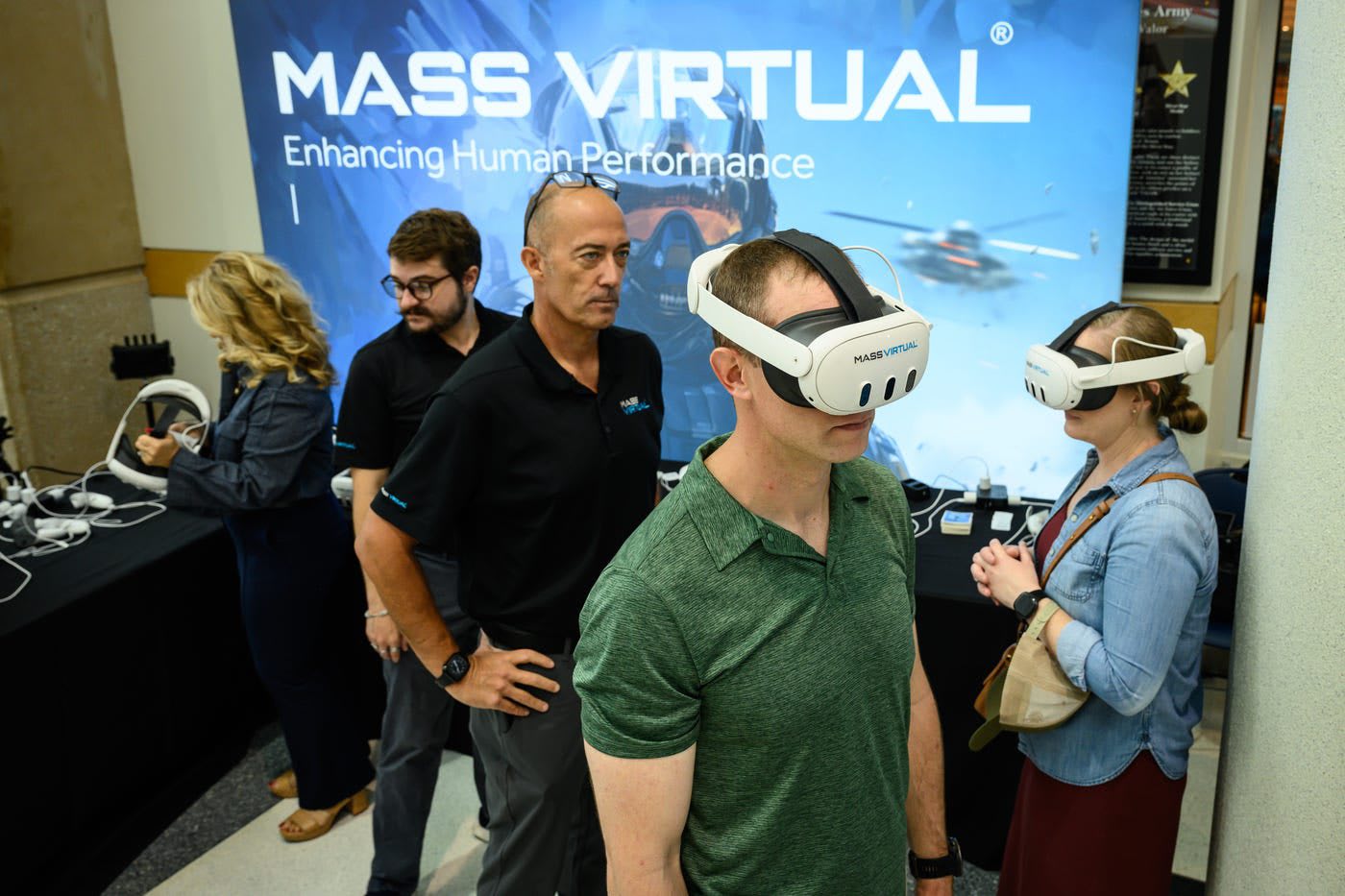 Museum visitors wearing white VR headsets branded Mass Virtual at a demonstration table inside the Airborne & Special Operations Museum, in front of a large Mass Virtual banner.