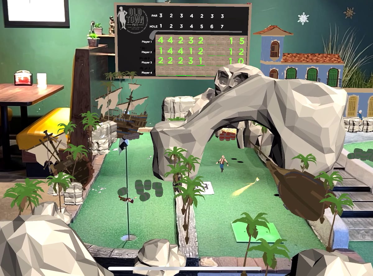 Pirate-island augmented reality scene overlaid on a hole at Old Town Putt, with a virtual ship, rock arch, pirate characters, barrels and the venue's in-game scoreboard