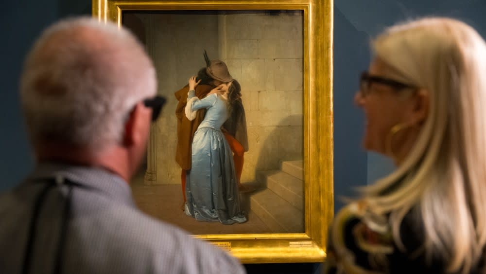 Two visitors wearing glasses stand in front of Francesco Hayez's painting The Kiss at Pinacoteca di Brera.