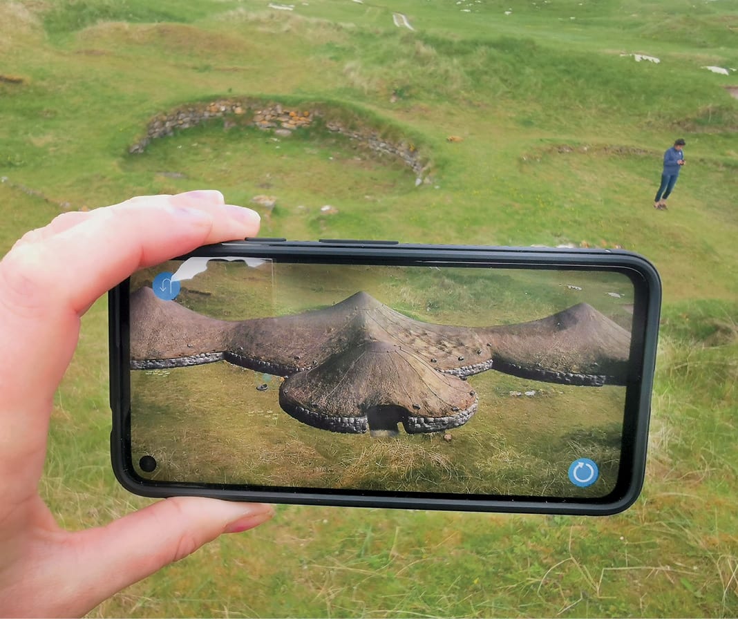 The Bronze Age roundhouses at Cladh Hallan reconstructed in augmented reality, viewed through a smartphone held up at the excavated site