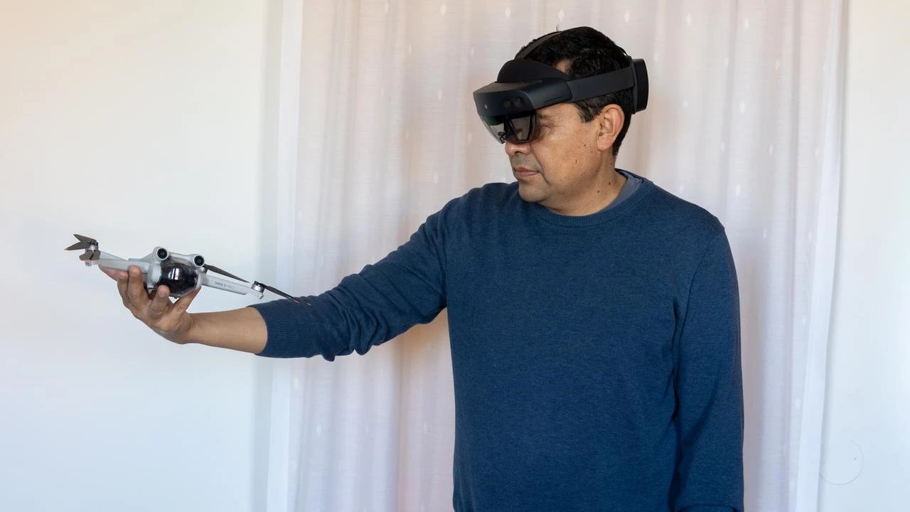 A man wearing a Microsoft HoloLens 2 mixed reality headset holds a small drone out at arm's length.