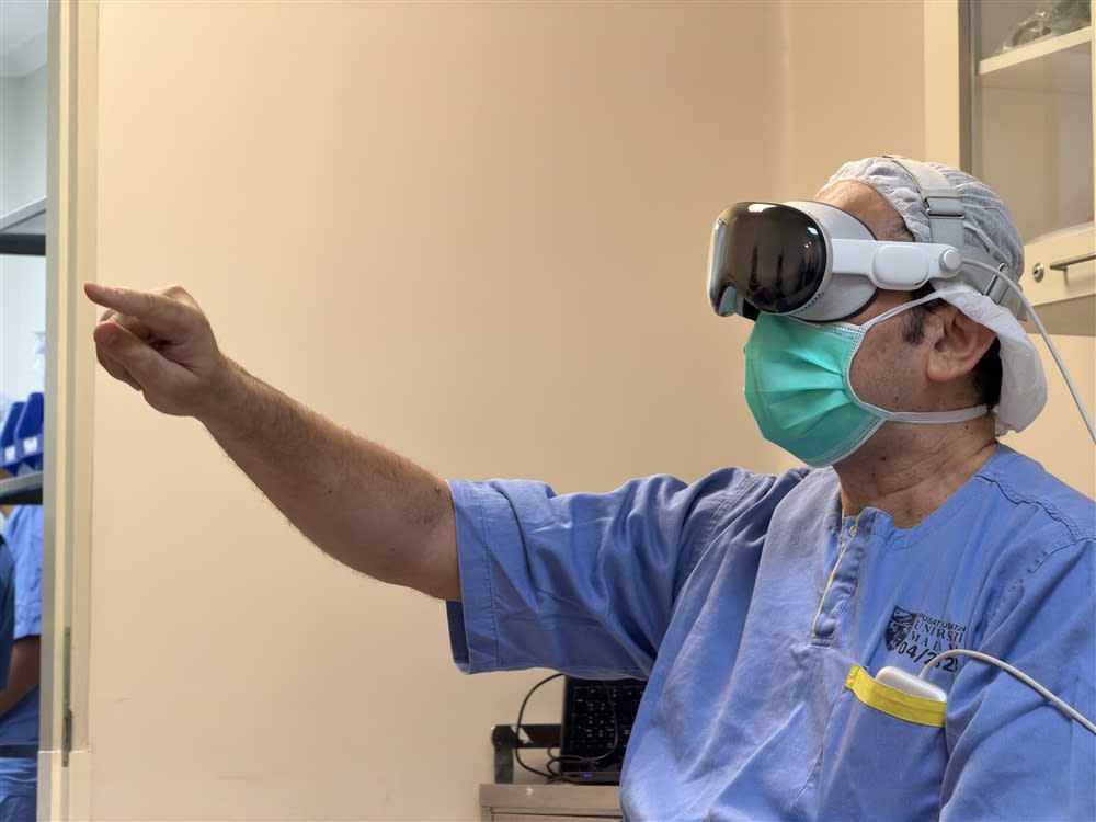 A clinician in Universiti Malaya scrubs wearing a mixed-reality headset in the UMMC operating theatre during the live-streamed procedure.