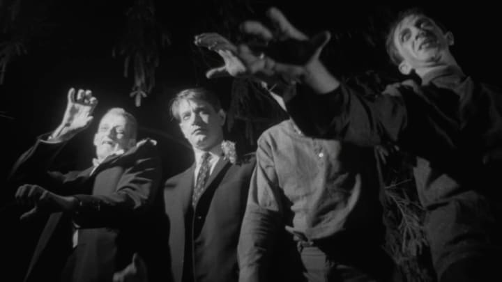 A black and white image of four zombified men reaching out towards the screen. They are well dressed and have neutral expressions