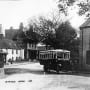 Black and white postcard of St Peter's Village with old bus at bus stop.