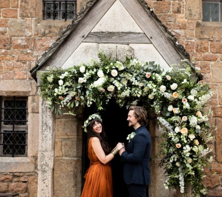 Hamptonne Man and Woman outside building with flower arch