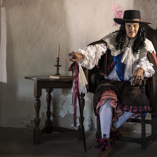 Man dressed as King Charles II sits and stares into camera