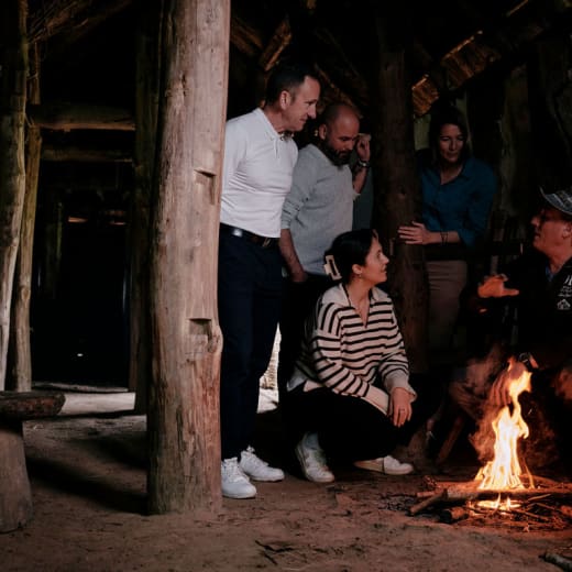 four people watch a heritage volunteer making fire