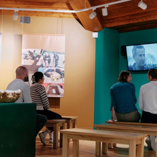 Four people sit and watch a video in an exhibition space