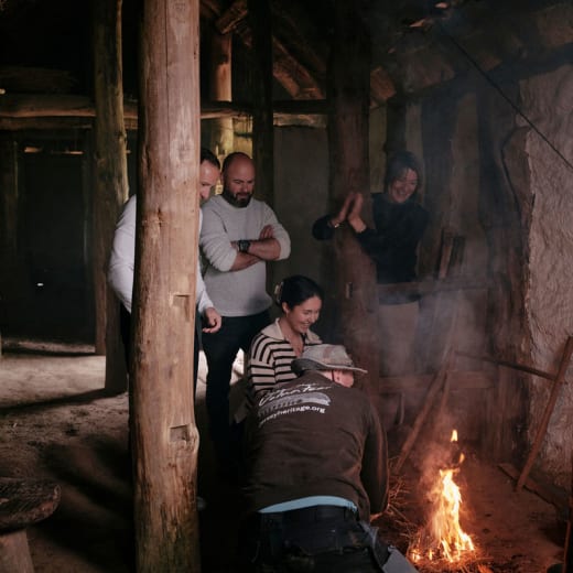 Group of four watch a man use traditional techniques to start a fire