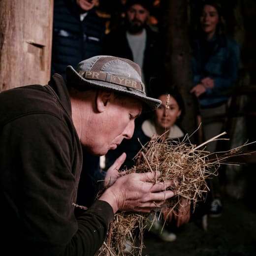 Group watches a man blow on straw to start a fire