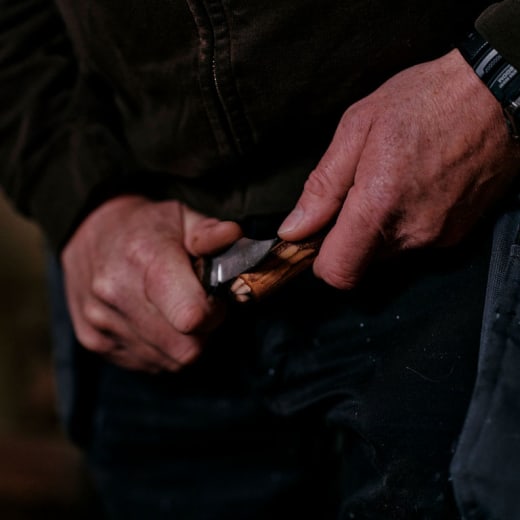 Close up of hands as a knife shaves wood chips