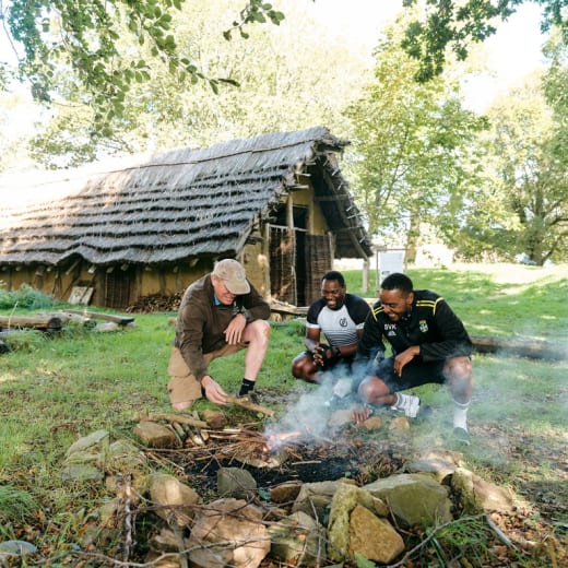 Two men watch someone set a fire int he outdoor