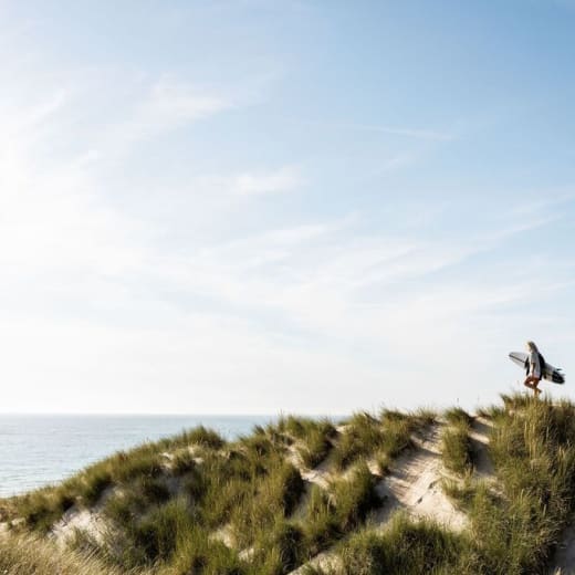 Two surfers walk across sand dunes