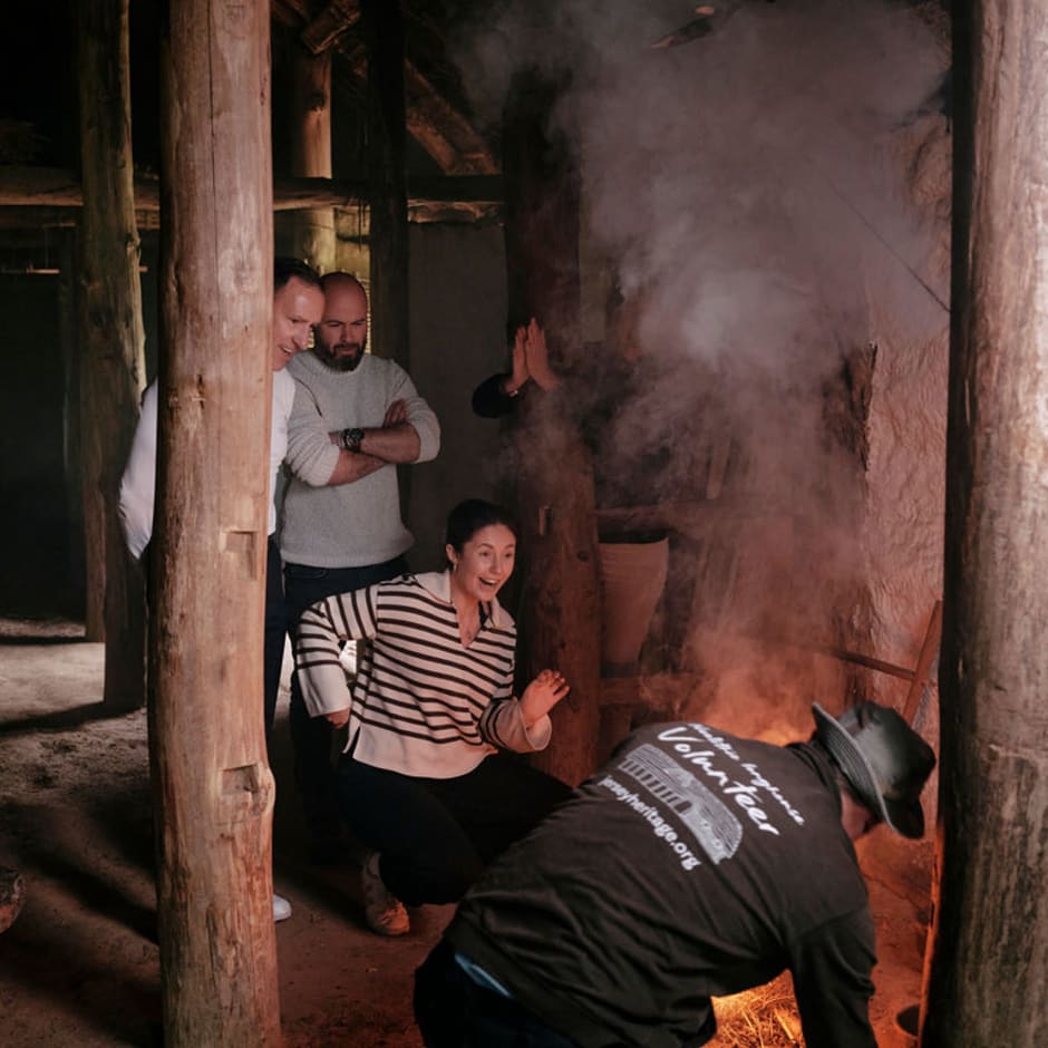 Group stands and watches a man light a fire