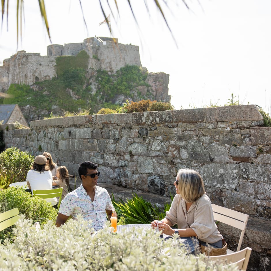 man and woman sit at an outside cafe with a castle in background