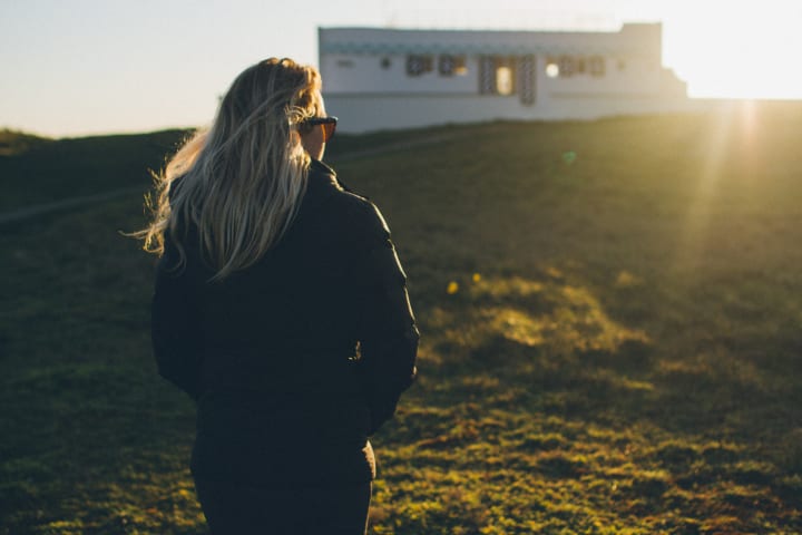 Woman walks towards a house with the sunrising in the distance