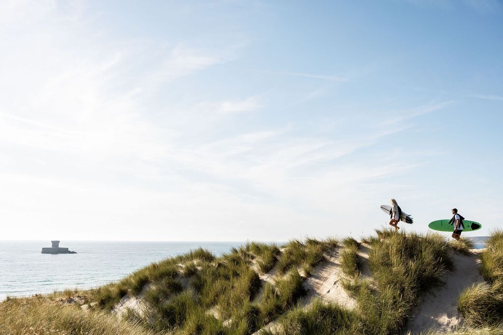Two surfers walk across sand dunes