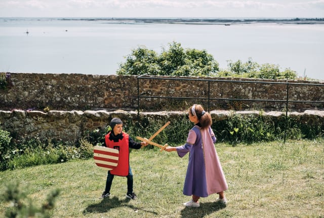 Two children dressed up as knights and princesses play in the garden
