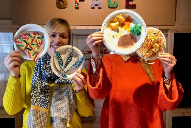 Two people hold us plates of paper food behind a sign saying Make Space