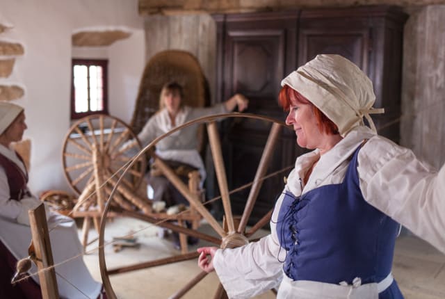 Woman in 17 century clothing sits at spinning wheel