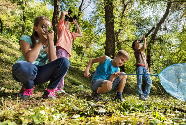 Young family squat on woodland ground hunting for wildlife with camera and net