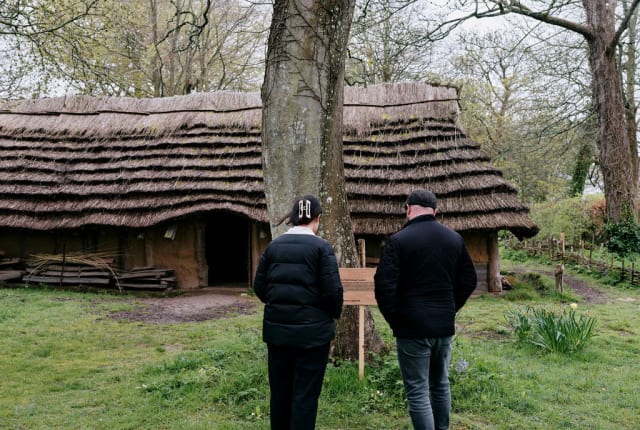 Two people read sign inf front of a replica neolithic longhouse