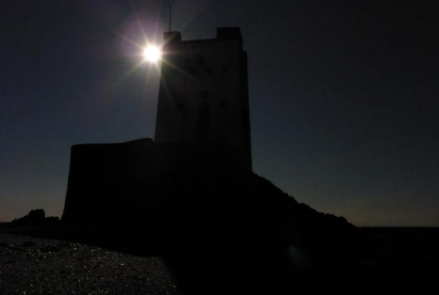 A bright moon shines behind a tower