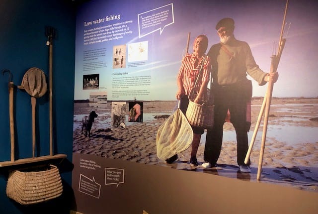 Exhibition panels show a couple on a beach with basket and long poles