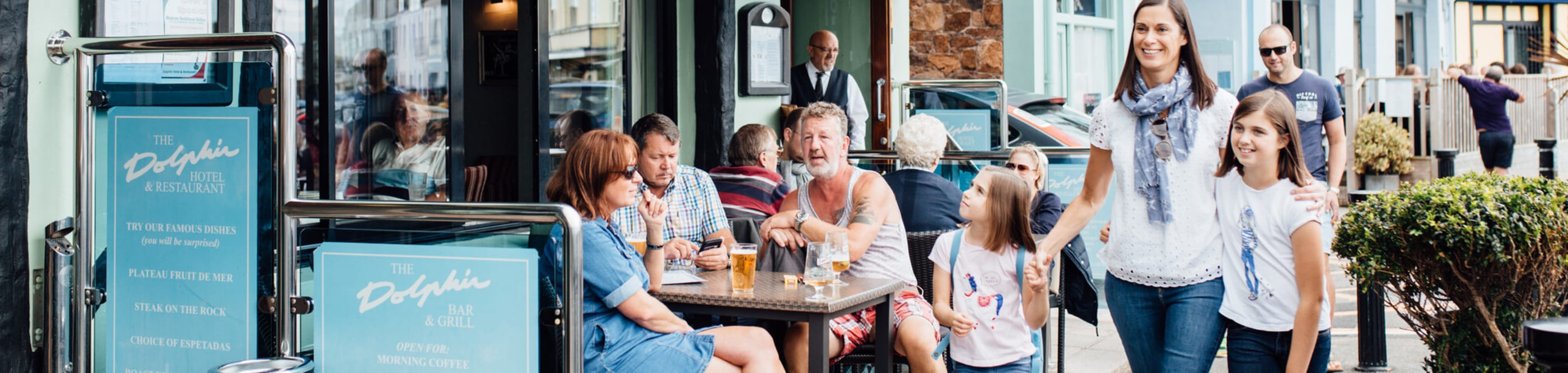 Family walk past a busy pup with people drinking outside.